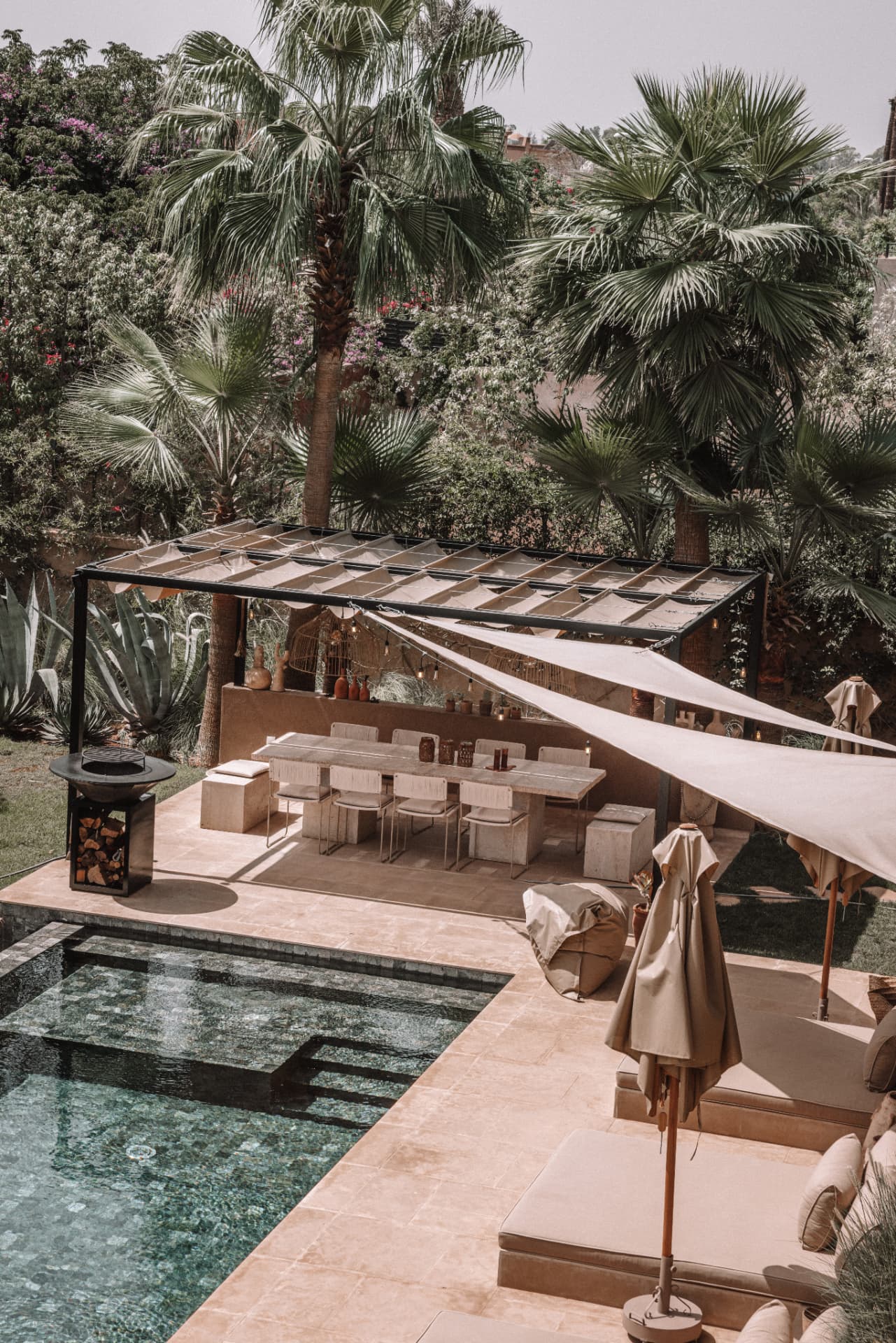 Outdoor dining room under a shaded pergola, travertine table and armchairs beside the pool